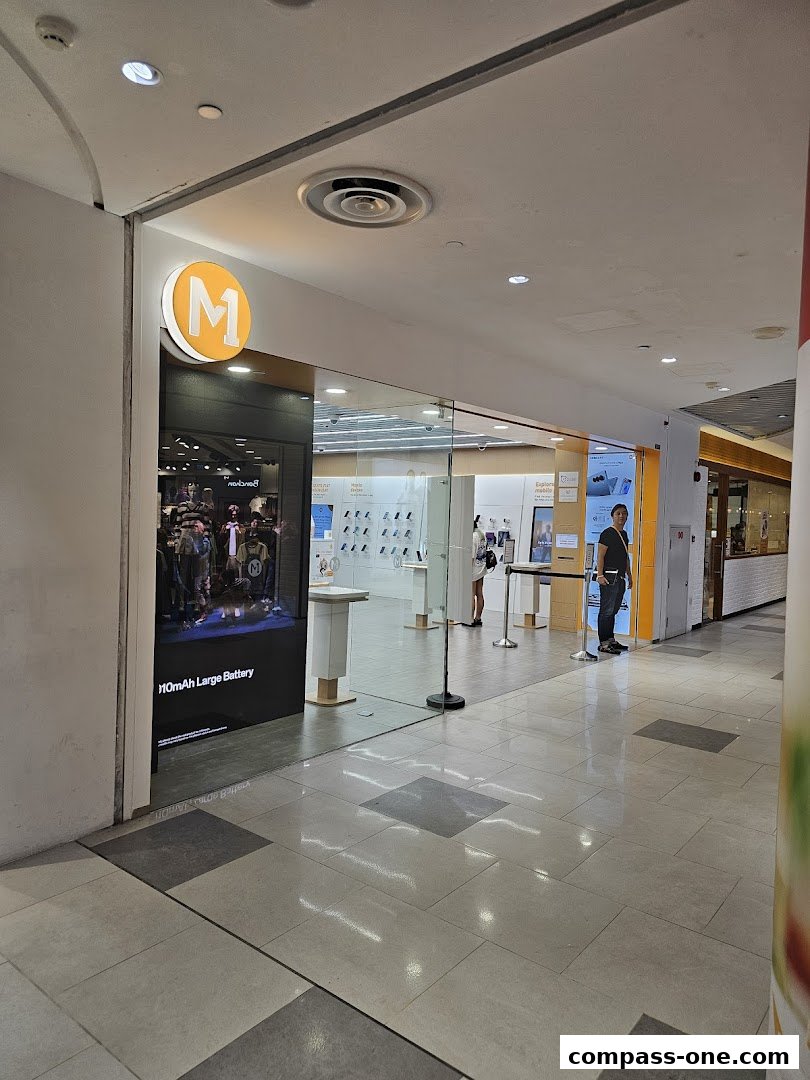 The entrance of a modern phone shop with a prominent 'M' logo and displays of mobile phones.