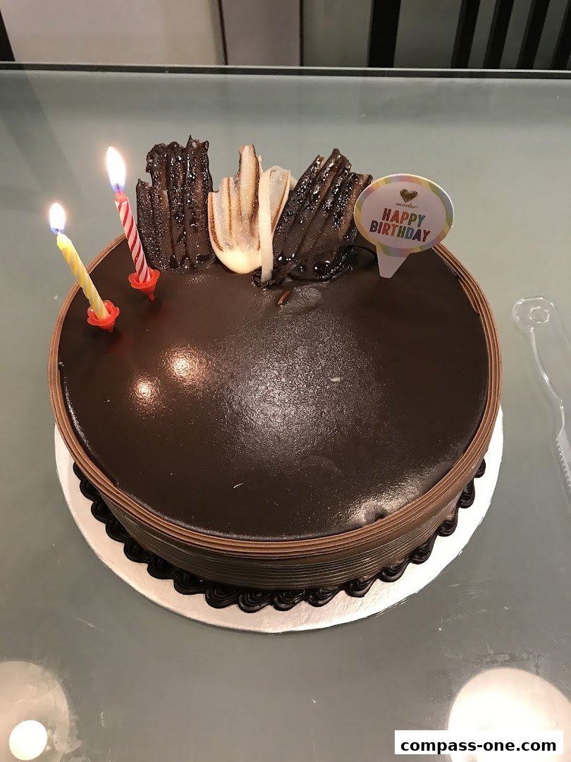 A decadent chocolate cake with lit birthday candles and decorative chocolate pieces.