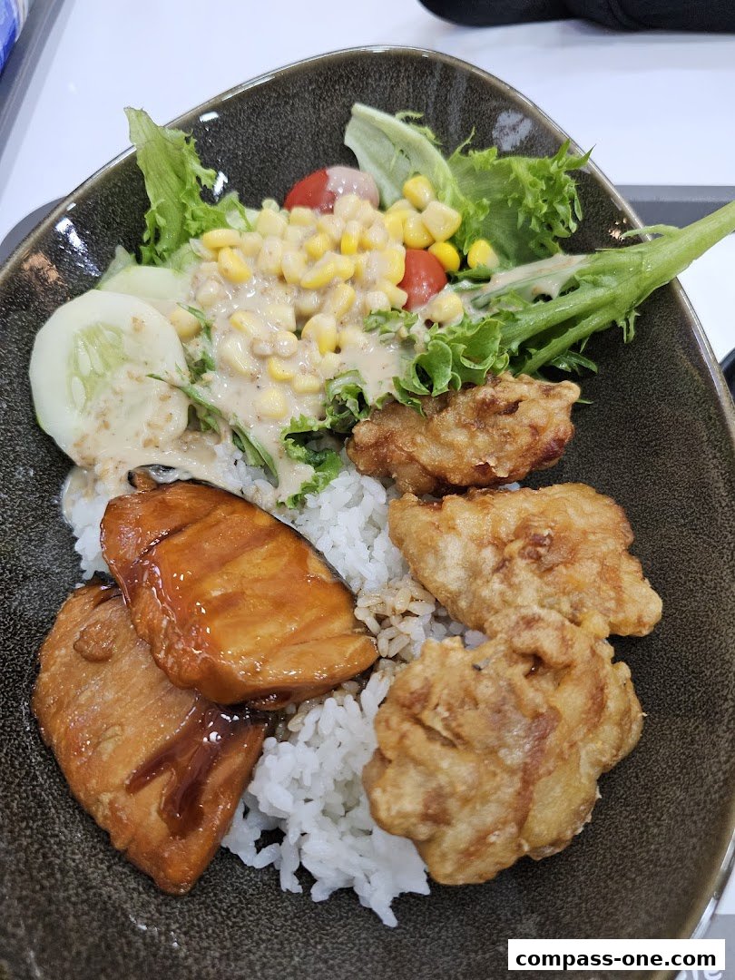 A close-up of a Yoshinoya meal featuring teriyaki salmon, fried chicken, rice, and a fresh salad.