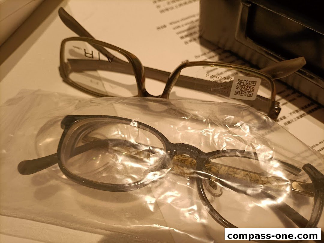 Two pairs of eyeglasses, one in a plastic bag, are displayed on a surface with text.