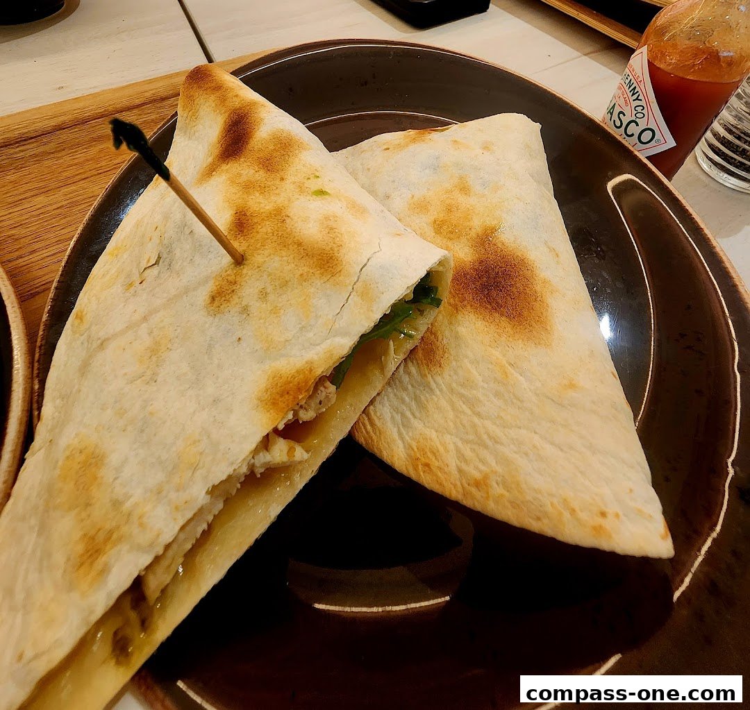 A close-up shot of a delicious quesadilla served on a dark plate with a bottle of Tabasco sauce.