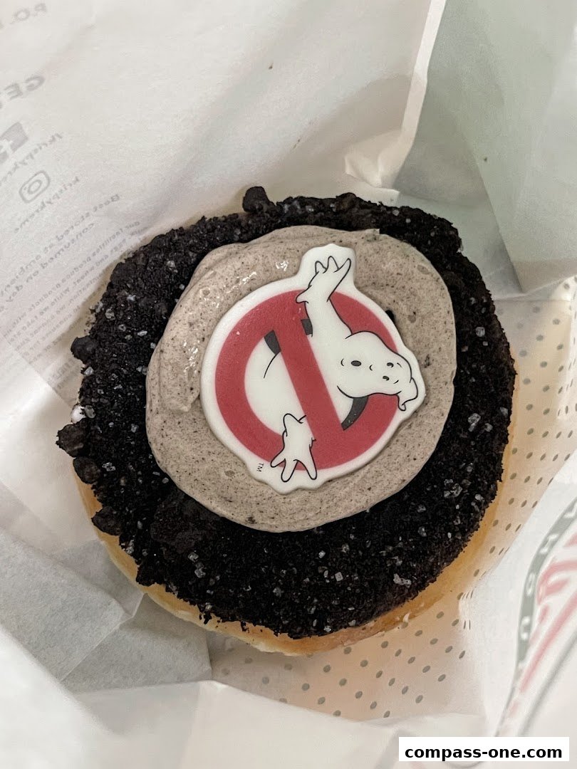 A close-up of a Krispy Kreme donut with cookies and cream frosting and a Ghostbusters logo.