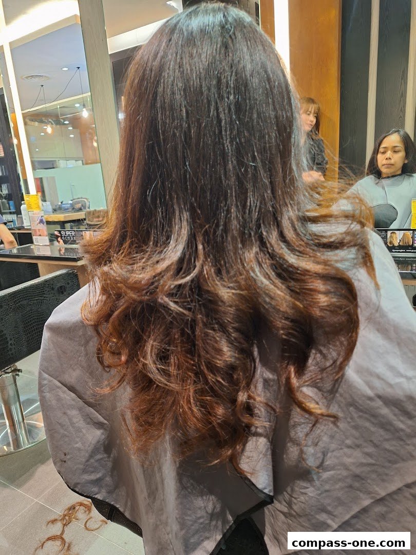 A person's back with long, wavy brown hair being styled in a salon.