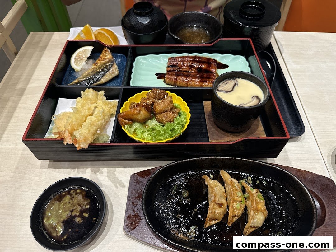 A bento box with various Japanese dishes and pan-fried dumplings on a sizzling plate.