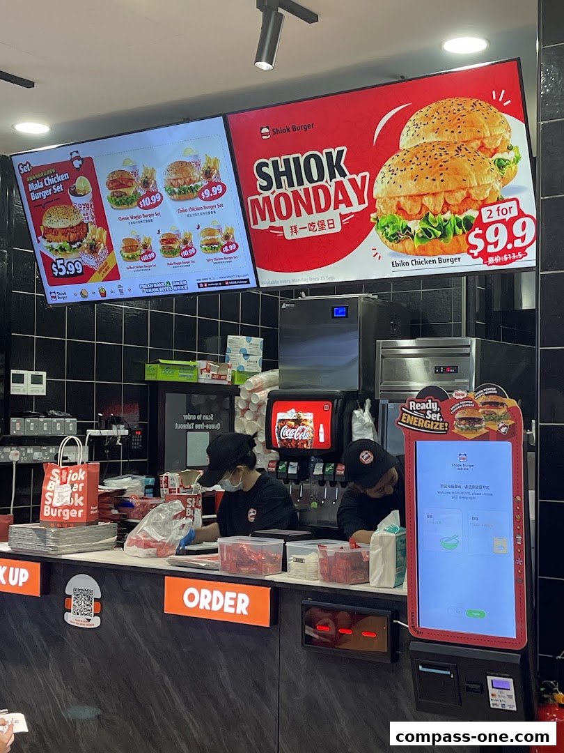 A view of the Shiok Burger counter with digital menus displaying burgers and staff preparing orders.