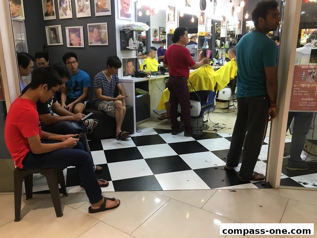 Customers wait at a busy barbershop with stylists cutting hair and photos of hairstyles on the wall.