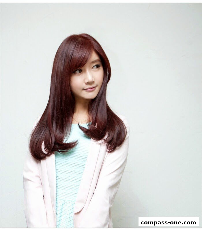 A young woman with long, auburn hair and a light pink blazer poses against a white background.
