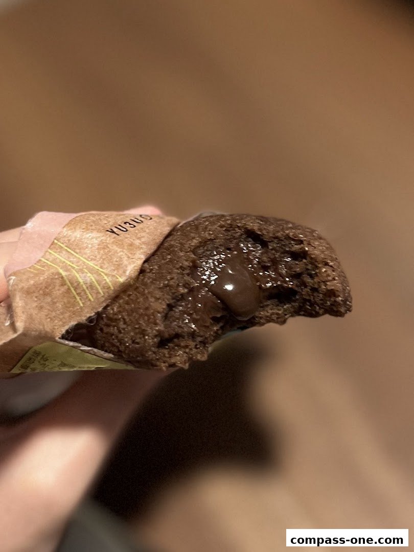 A hand holds a chocolate muffin with a gooey chocolate filling.