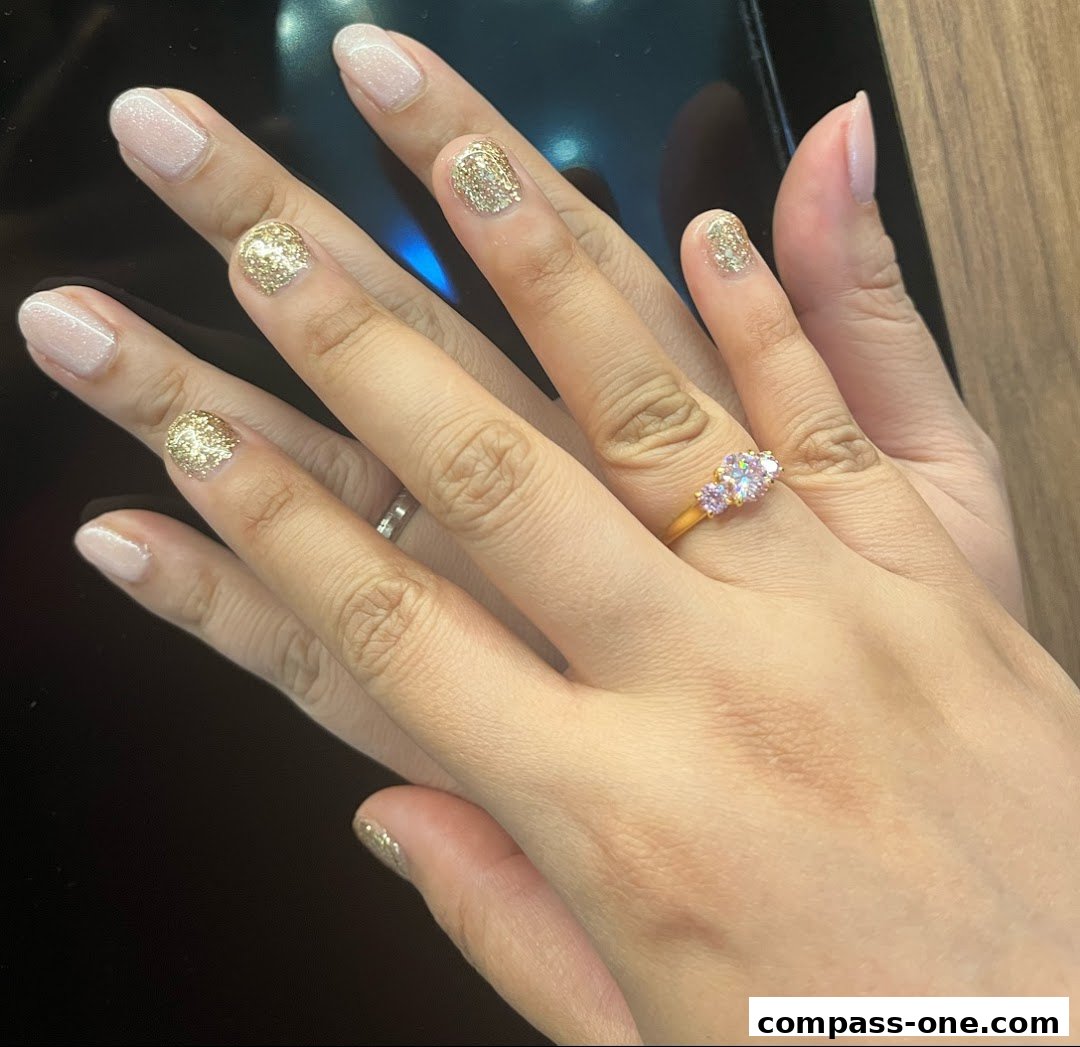 A close-up of hands with a glitter and nude nail polish, wearing a ring.