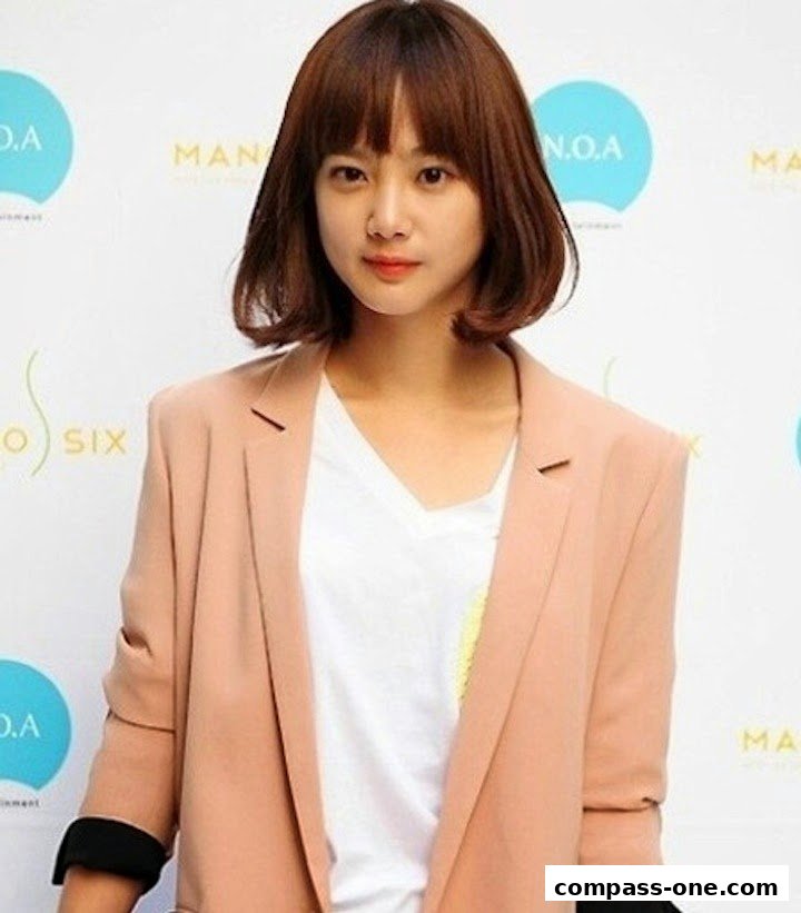 A woman with a bob haircut and bangs wears a peach blazer over a white t-shirt.
