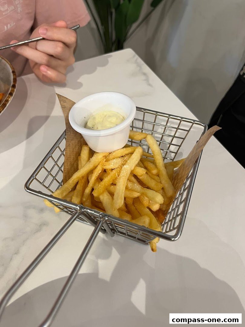 A basket of golden french fries with a side of dipping sauce is presented on a white table.