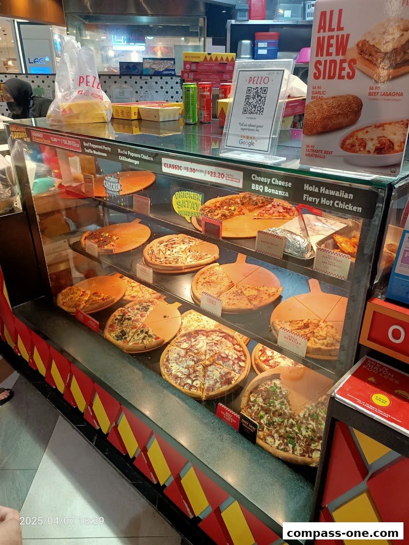 A display case filled with various pizzas and sides at Pezzo Compass One.