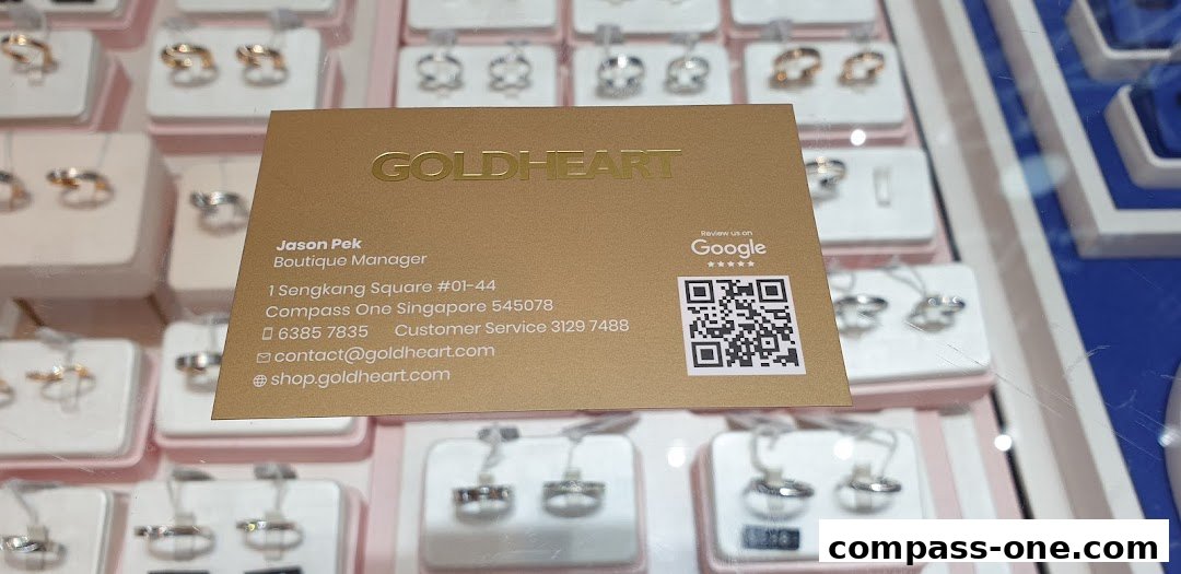 A business card for Goldheart jewelry store is displayed in front of a jewelry display case.