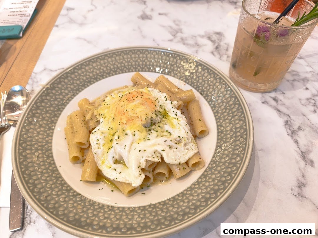 A plate of rigatoni pasta topped with a fried egg and cheese, next to a cocktail.