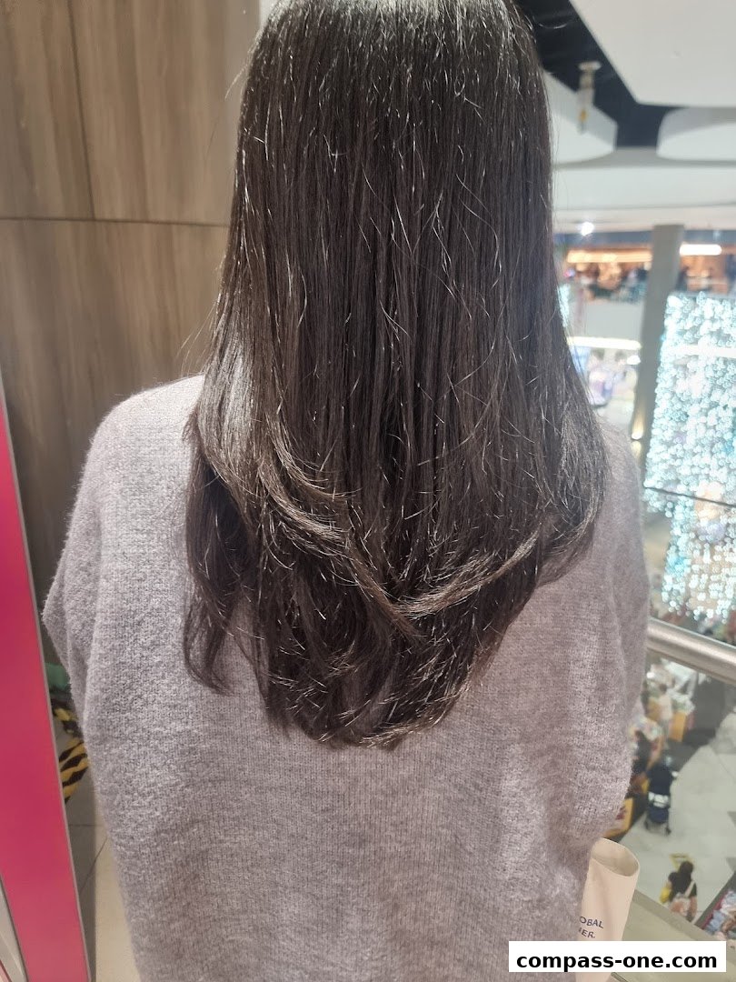 A person's back with long, dark, layered hair, wearing a grey sweater.
