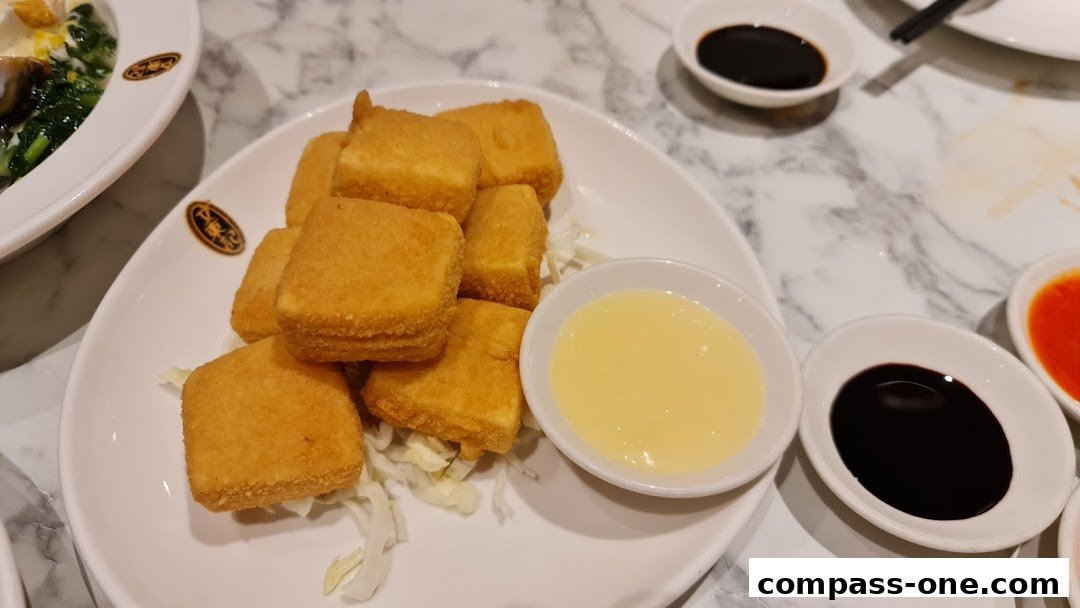 A plate of golden fried tofu cubes served with dipping sauces and a side of shredded cabbage.