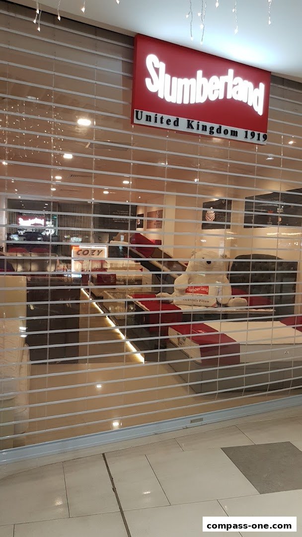 Slumberland COZY BEDDING CO shop front with a closed roller shutter and a large teddy bear.