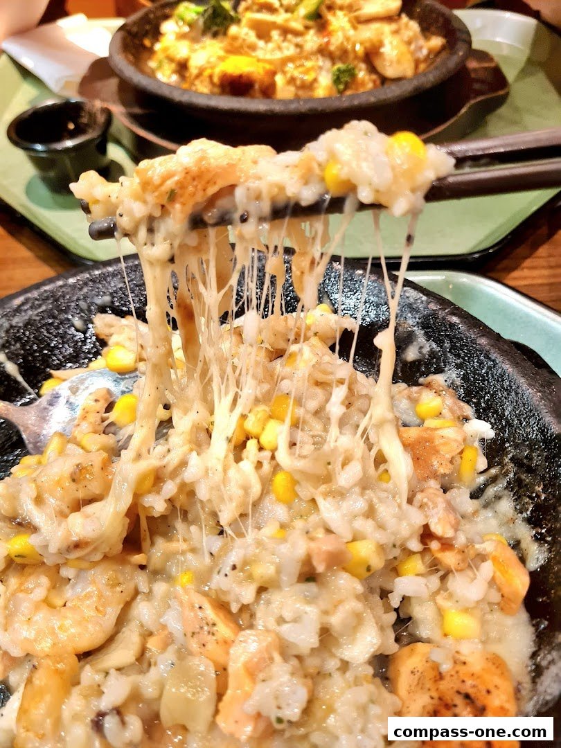 A close-up of a cheesy rice dish with salmon and corn, being lifted by chopsticks.
