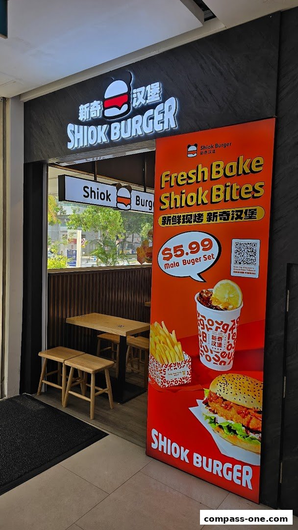 The entrance of Shiok Burger, featuring its logo, a promotional banner, and interior seating.