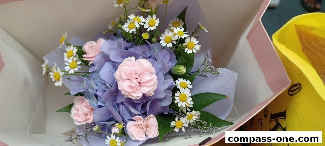 A beautiful bouquet of blue hydrangeas, pink carnations, and daisies in a pink and white gift bag.