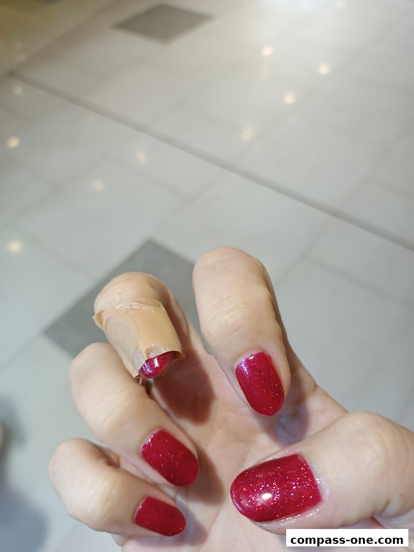 A close-up of a hand with bright red glitter nail polish and a band-aid on the index finger.