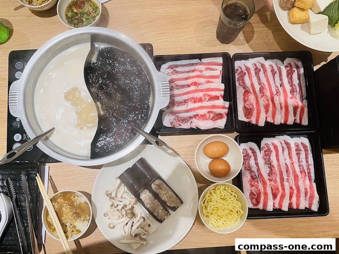 A table laden with a split hot pot, thinly sliced meats, eggs, noodles, and other ingredients.