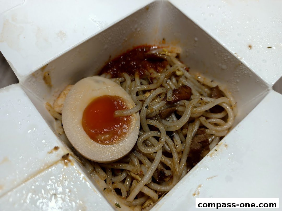 A close-up of a takeaway box filled with noodles and a perfectly cooked soft-boiled egg.