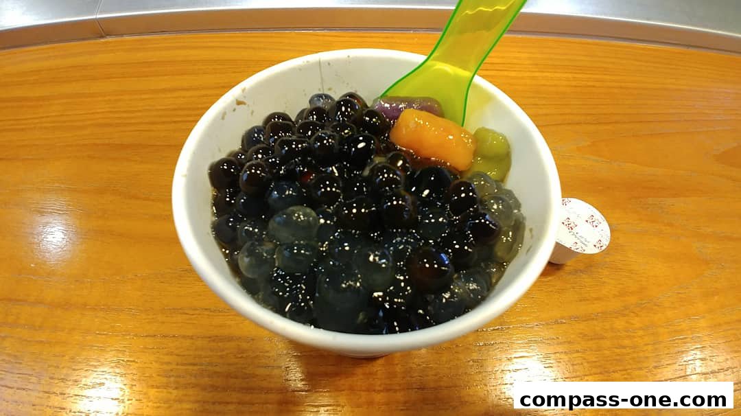 A bowl of bubble tea with various toppings and a green spoon on a wooden table.