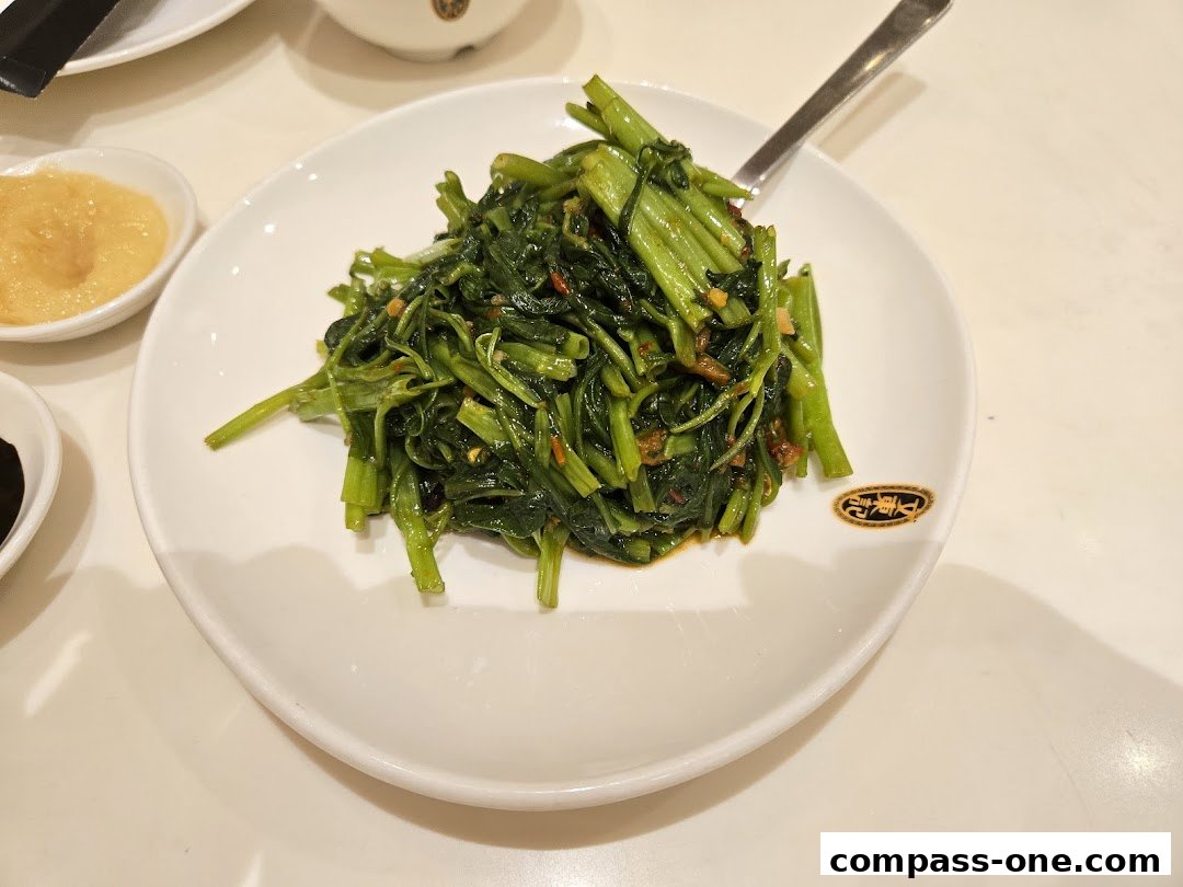 A plate of stir-fried water spinach with chili and garlic, served with dipping sauces.