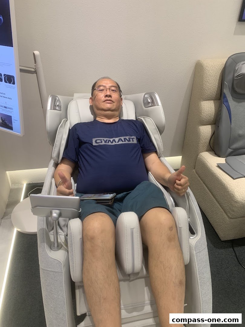 A man sits in a massage chair, giving a thumbs up, with another chair visible.
