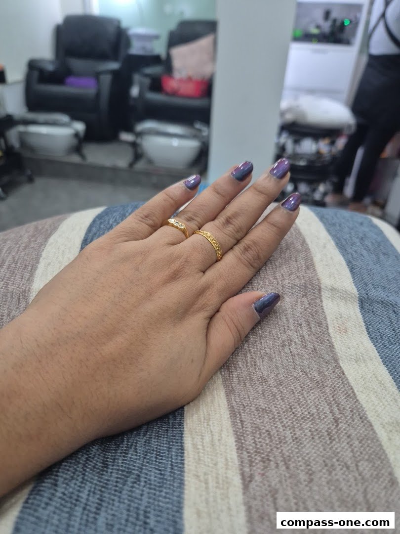 A close-up of a hand with purple and blue ombre nails and gold rings.