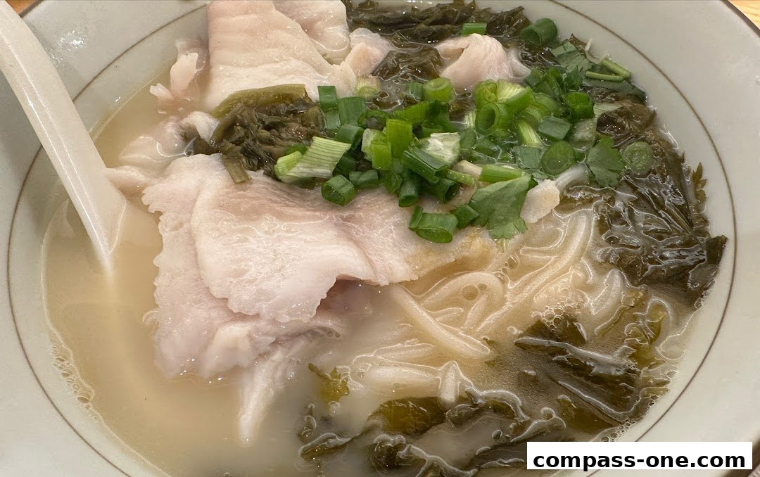 A close-up shot of a steaming bowl of noodle soup with fish slices, pickled vegetables, and scallions.