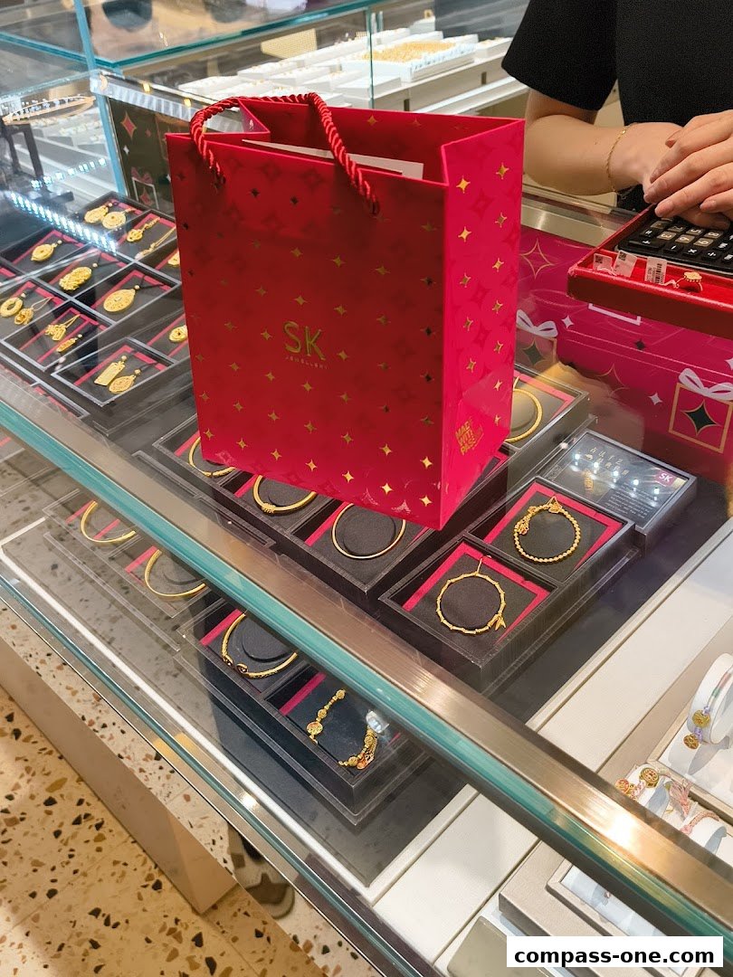 A red SK Jewellery shopping bag sits on a display case filled with gold jewelry.
