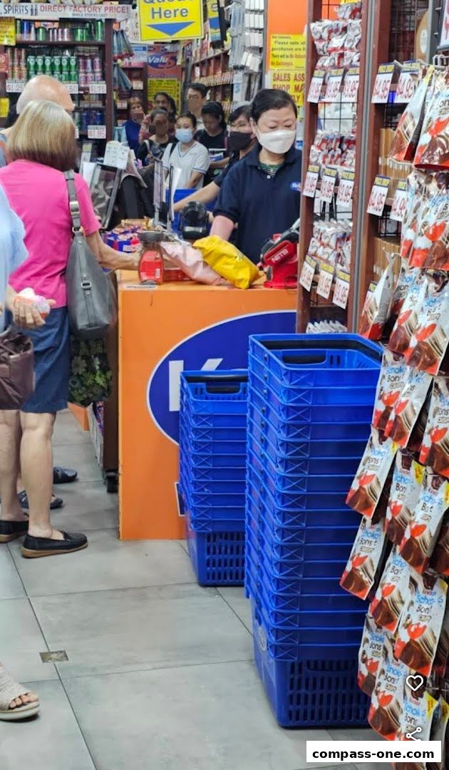 Customers queue at a checkout counter in a busy retail store with stacked blue baskets.