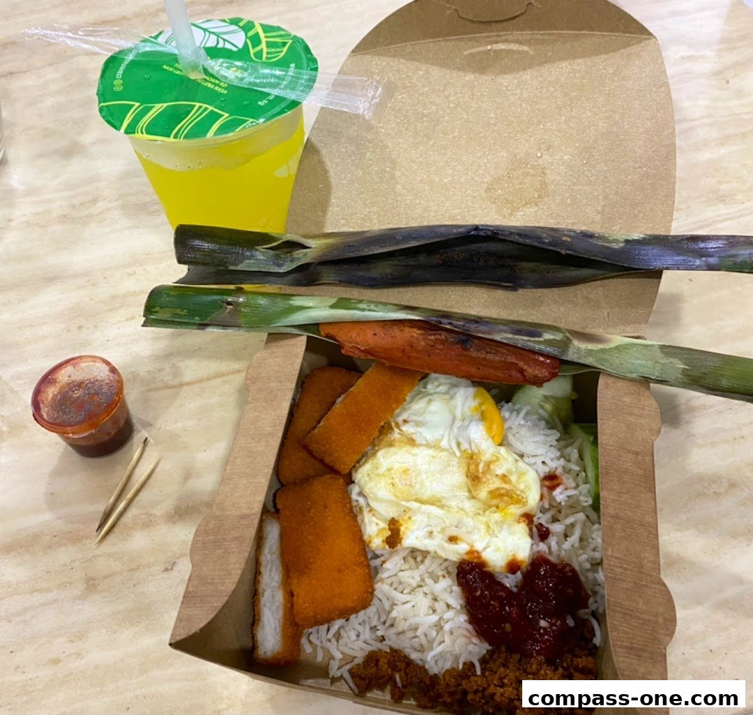 A takeaway box filled with nasi lemak, fried chicken, and a drink.