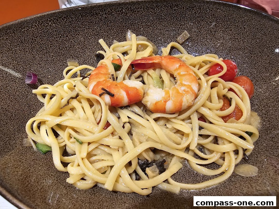 A close-up shot of a pasta dish with shrimp and cherry tomatoes in a textured bowl.