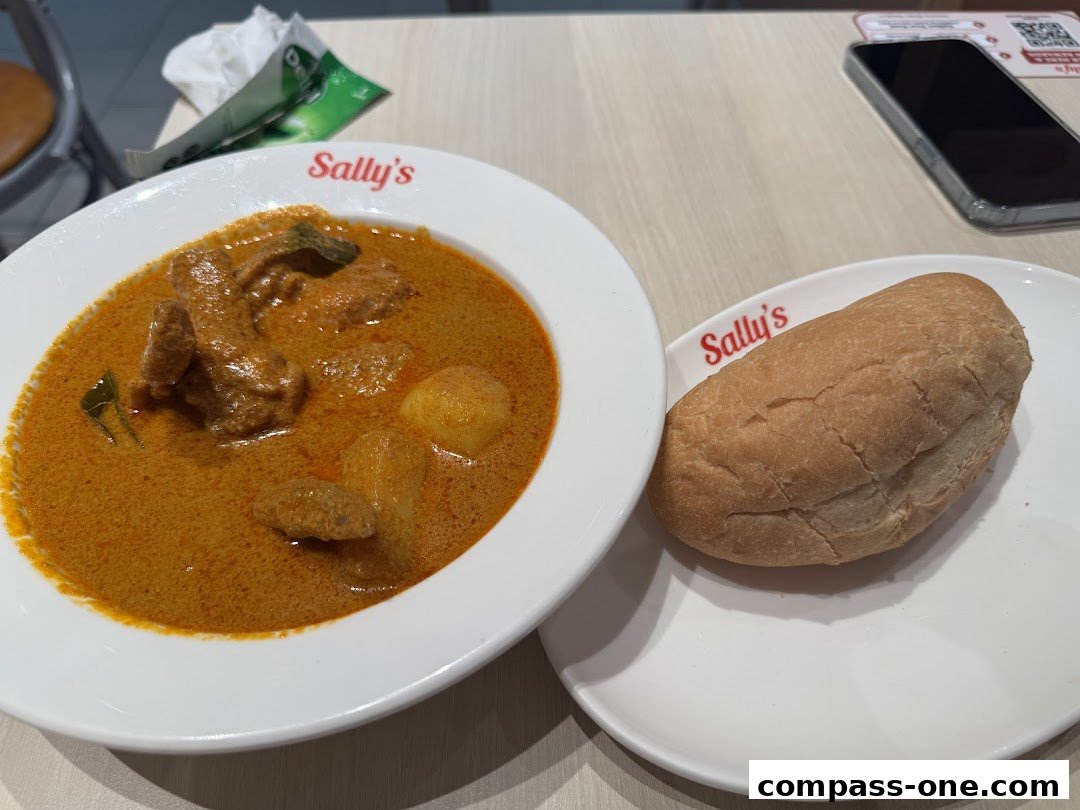 A bowl of curry with chicken and potatoes served with a bread roll at Sally's.
