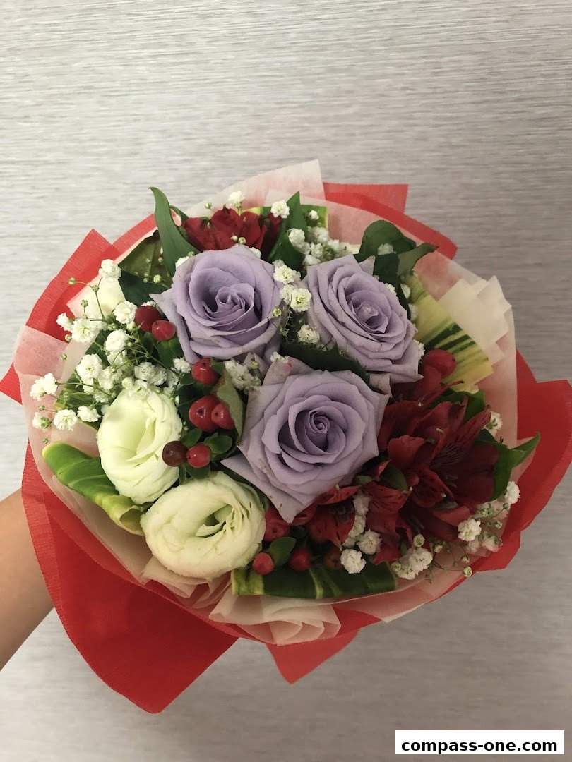 A hand holding a beautiful bouquet of purple roses, white lisianthus, and red accents.