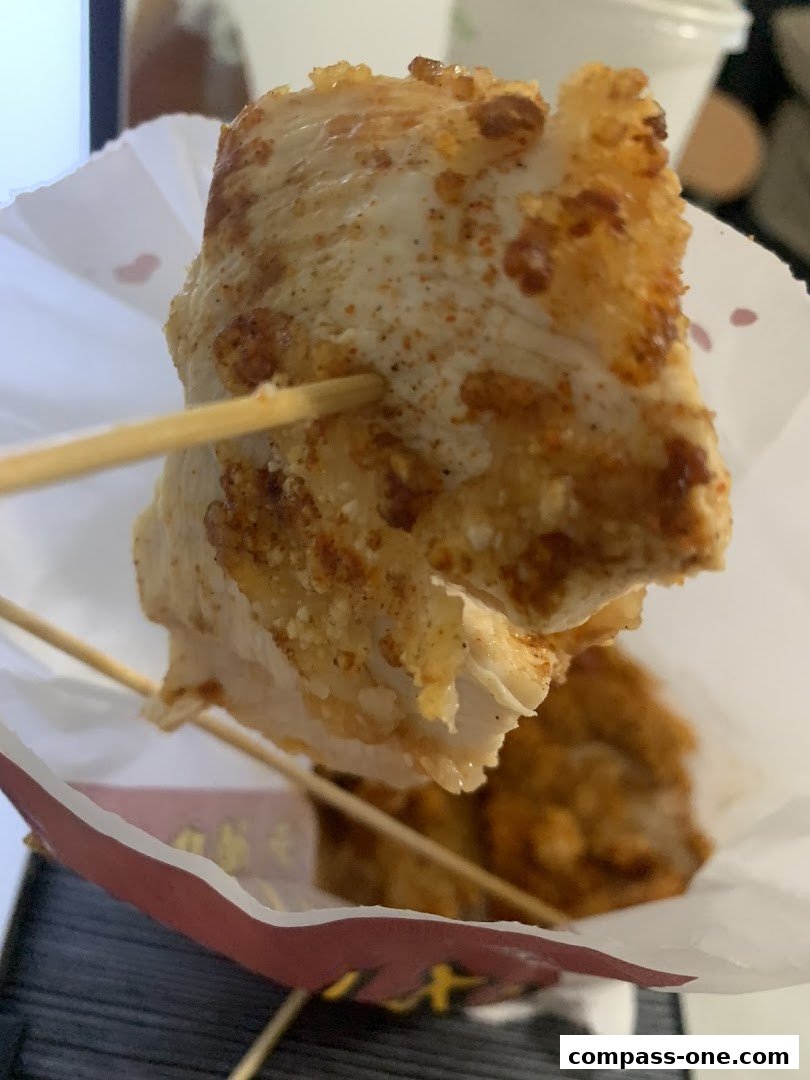 A close-up of a crispy, seasoned fried chicken piece on a skewer.