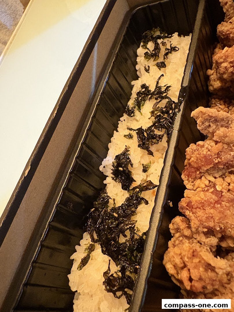 A close-up of a takeaway container with rice topped with seaweed and fried chicken.