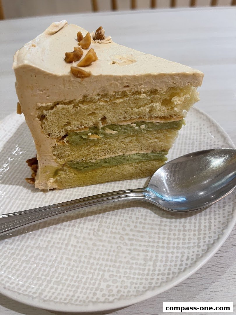A slice of layered cake with coffee frosting and nuts on a textured plate with a spoon.