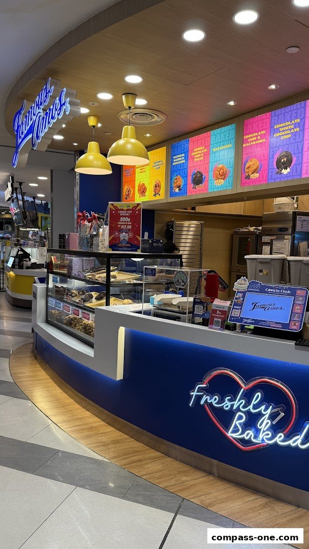 A Famous Amos cookie shop counter with freshly baked cookies displayed and a neon sign.
