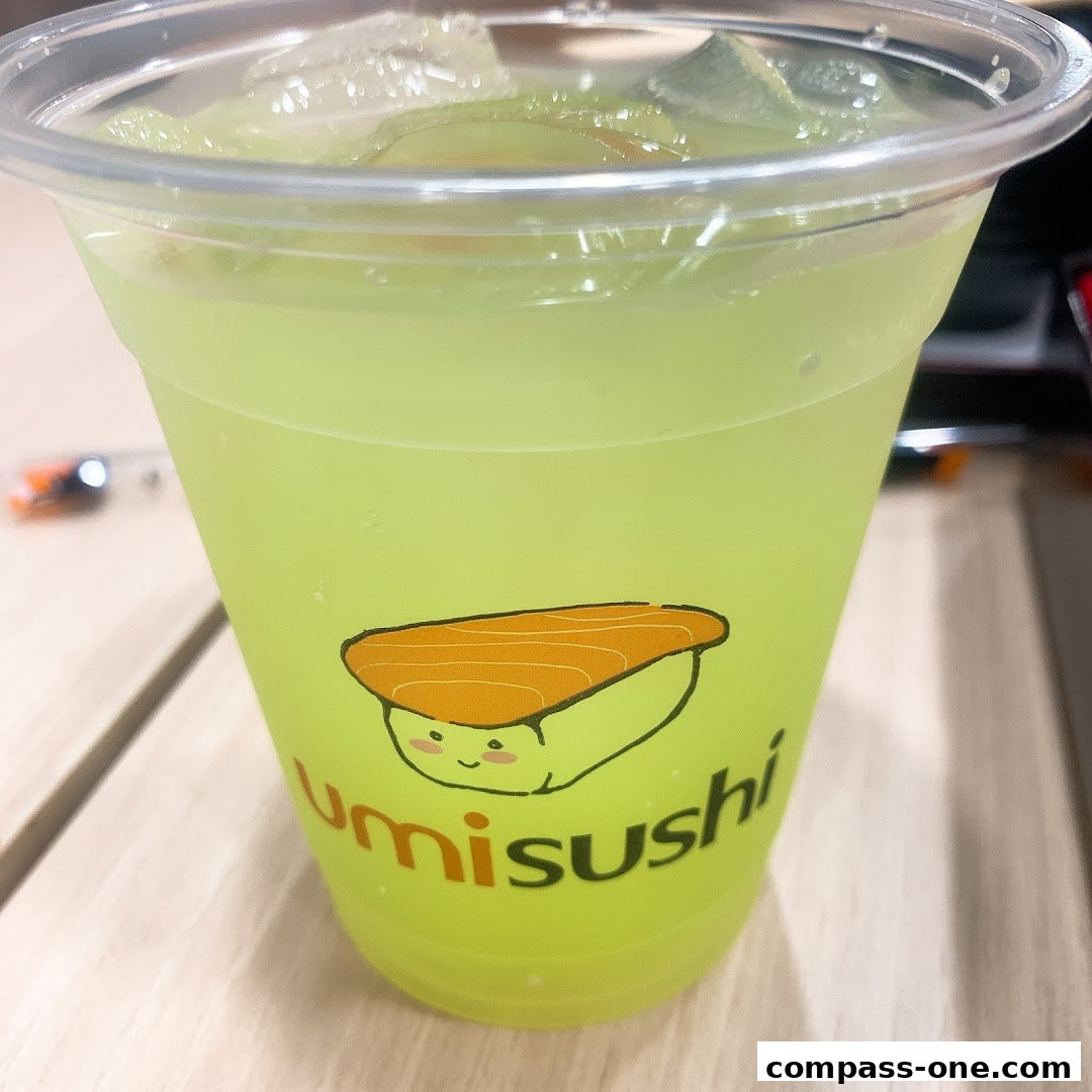A close-up of a bright green beverage in a clear plastic cup with the umisushi logo.