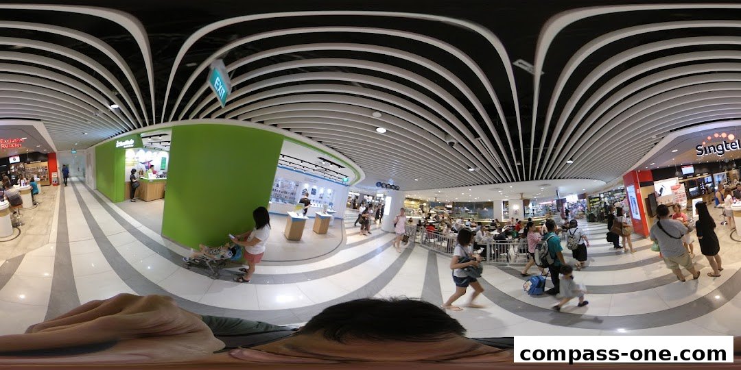 A panoramic view of a busy shopping mall with various shops and people.
