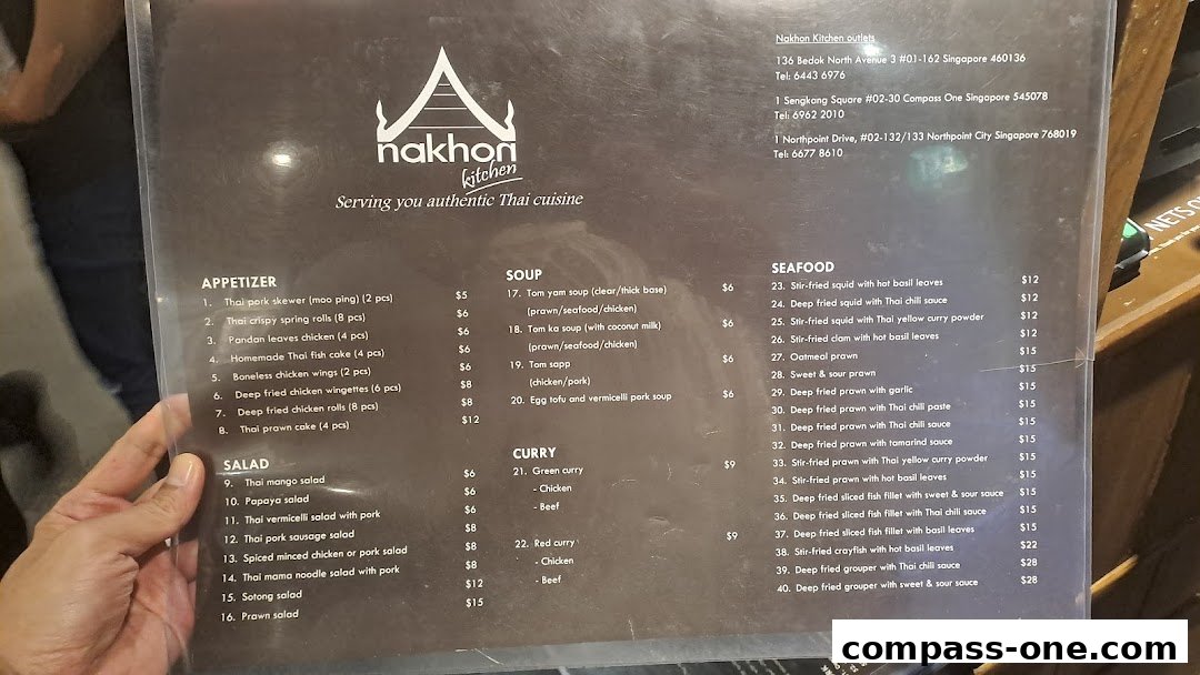 A person holds a menu for Nakhon Kitchen, showcasing authentic Thai cuisine with various categories and prices.