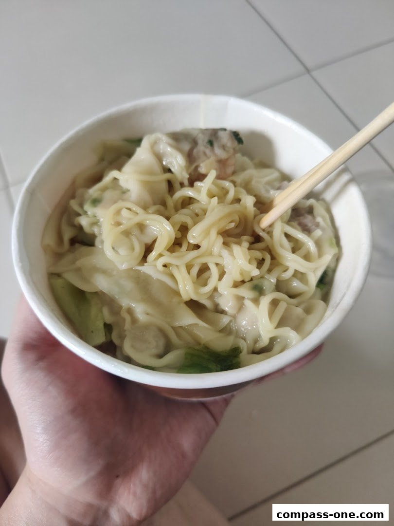 A hand holds a bowl of wonton noodles with chopsticks, showcasing a delicious meal.
