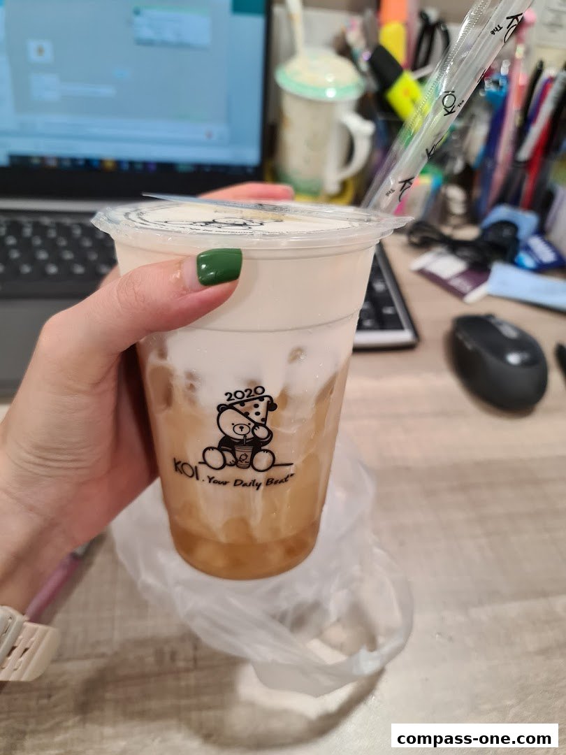 A hand holds a KOI Thé bubble tea with a creamy top and ice.