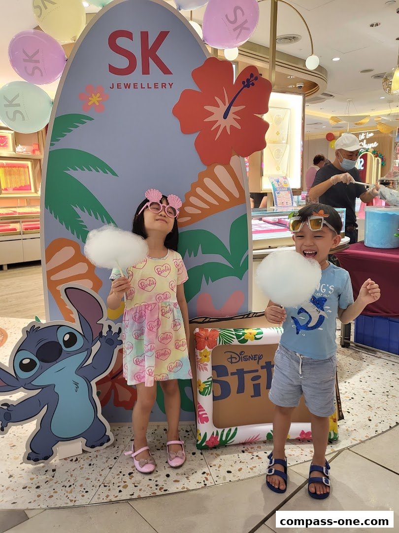 Two children enjoy cotton candy in front of a SK Jewellery display with Stitch.
