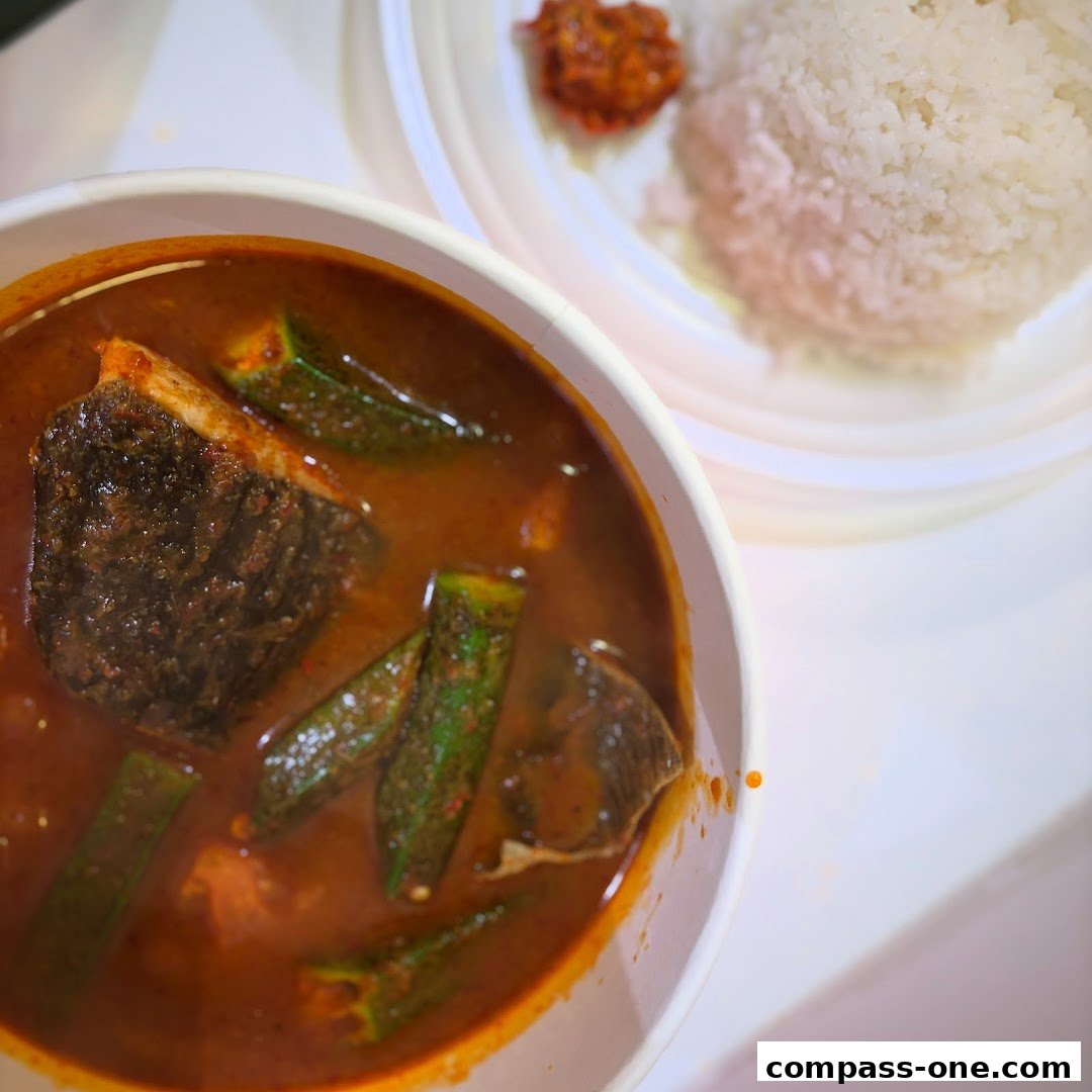 A close-up of a bowl of curry fish head with okra and a side of rice.