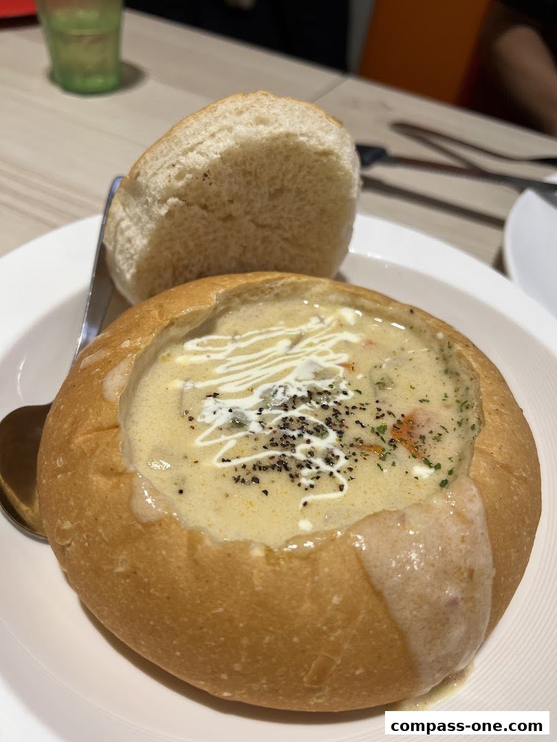 A creamy soup served in a bread bowl with a side bun and a spoon.